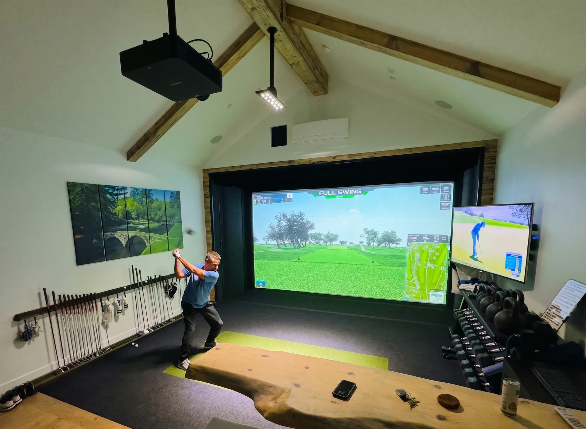 Golfer mid-swing in a vaulted-ceiling Full Swing simulator bay with a tracked screen, club rack, and live-edge counter